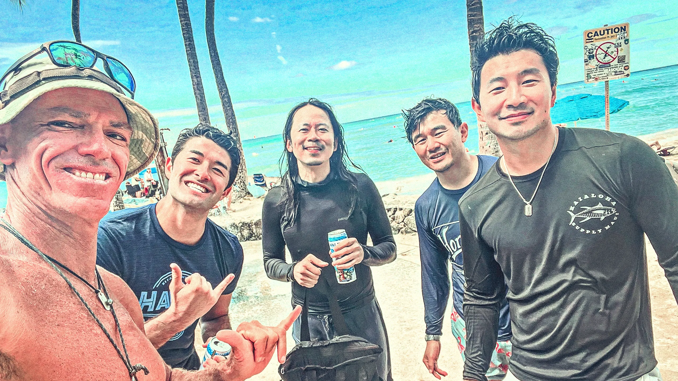 People paddleboarding and surfing on turquoise ocean water near a beach with tall buildings under a partly cloudy blue sky.